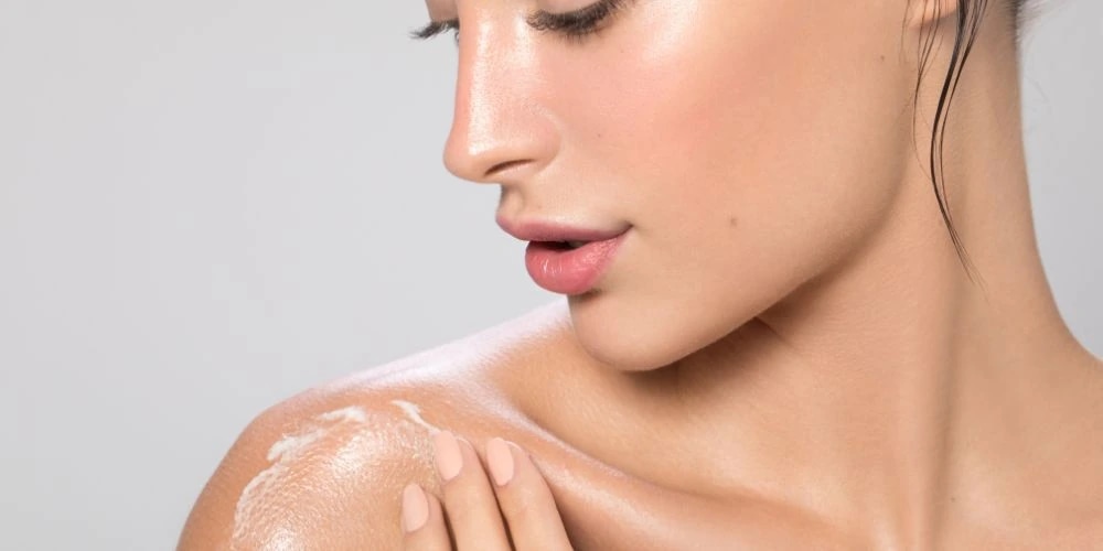 Face and arm of a woman who applies body balm to her shoulder.