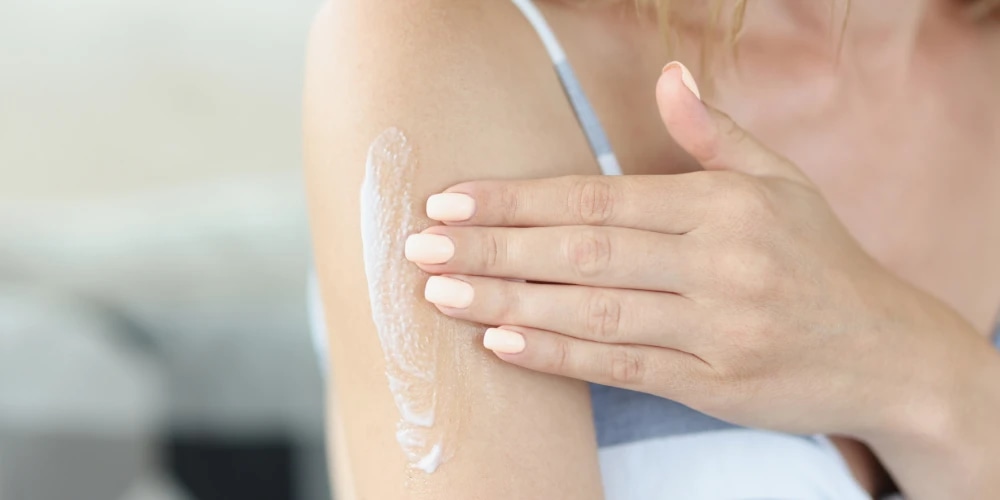 A woman applies body lotion to her tanned arm.